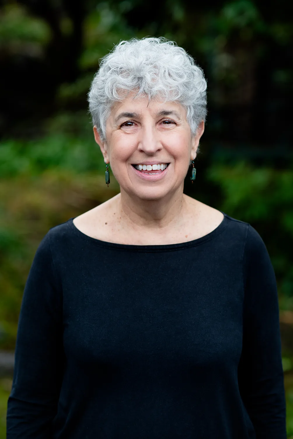 Rhea Tregebov, photo of the author in a black dress, in front of a blurred background of foliage